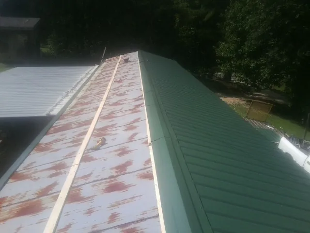 Old rusted panels beside newly installed green metal roofing — Wind Damage Roof Repair by Roofing Brothers in Wendell
