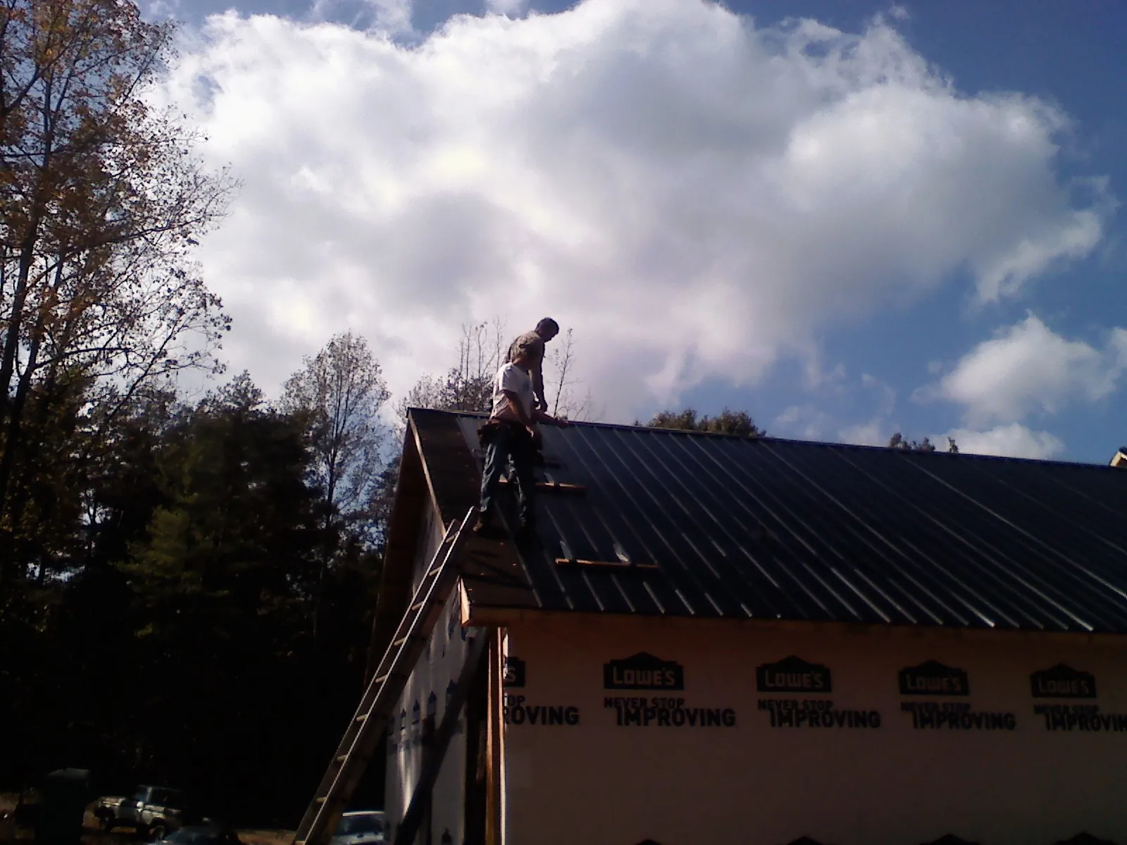 Roofer fastening dark metal panels high against a cloudy sky, from a Roof Inspection job in Wendell