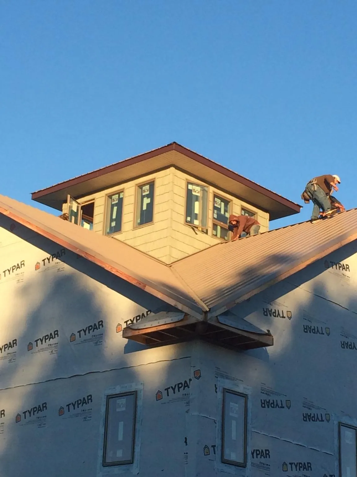 Roofers working around a rooftop cupola on a new metal roof at sunset — Roof Waterproofing in Wendell by Roofing Brothers